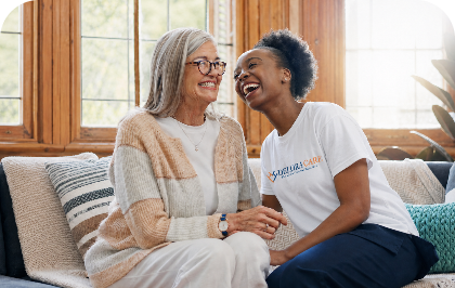 Delora Care caregiver and older adult smiling together on a sofa